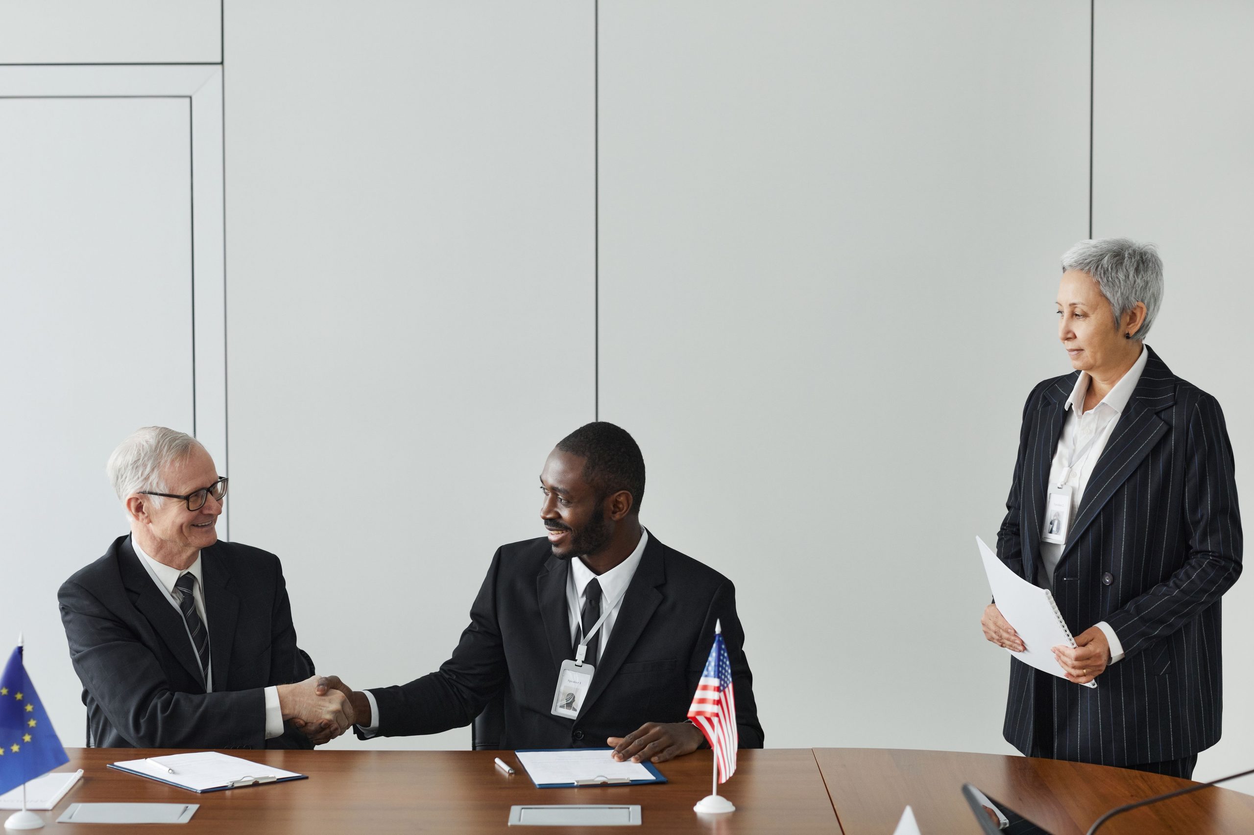 Multinational business meeting with agreement signing, featuring diverse professionals and international flags